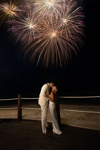 newlyweds kiss on beach below fireworks at Kimpton seafire